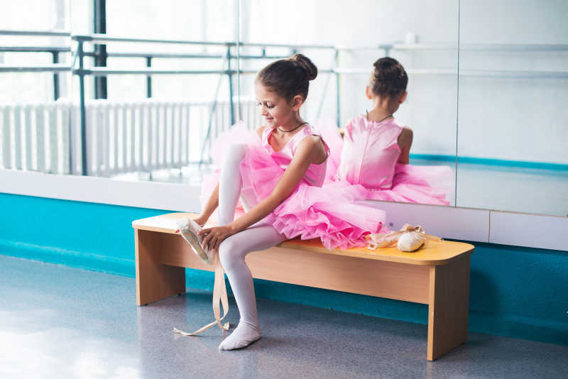 年轻的芭蕾舞女演员穿着粉红色的衣服坐在长椅上