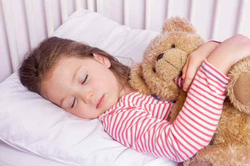 可爱的小女孩与毛绒玩具在她的床上睡觉