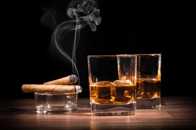 黑色背景威士忌酒杯和烟灰缸上的雪茄特写