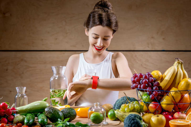 看表的女人面前放着新鲜的水果和蔬菜