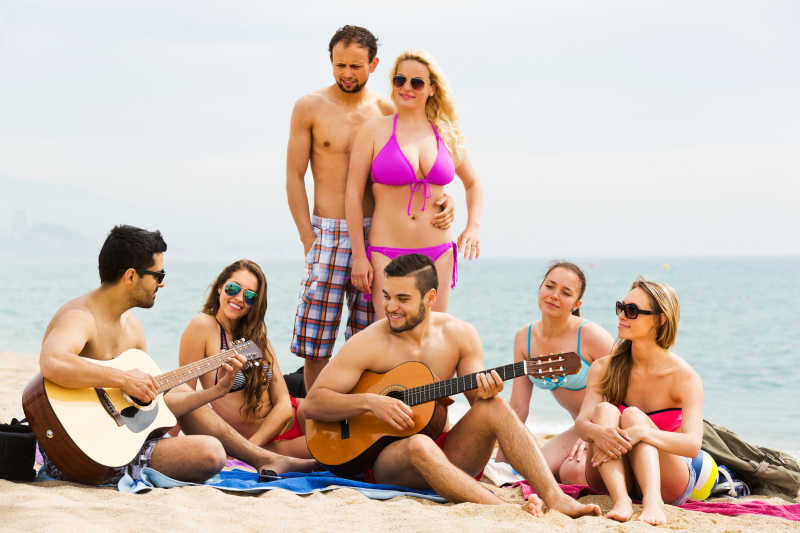 快乐的成年朋友在沙滩上悠闲地玩吉他和唱歌