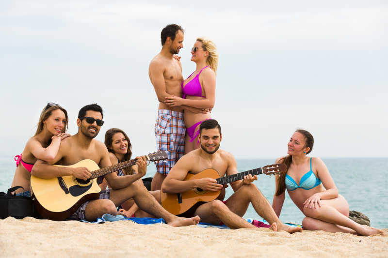 一群朋友在海滩上拿着吉它玩耍的朋友