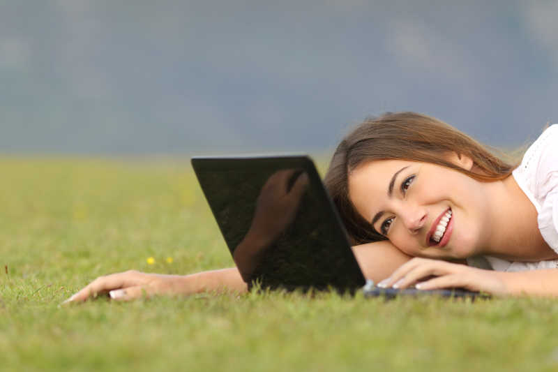 在草坪上使用笔记本电脑的快乐女人