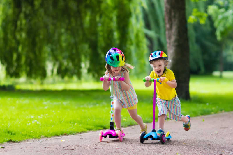 阳光明媚的夏日公园孩子们在公园里学骑滑板车