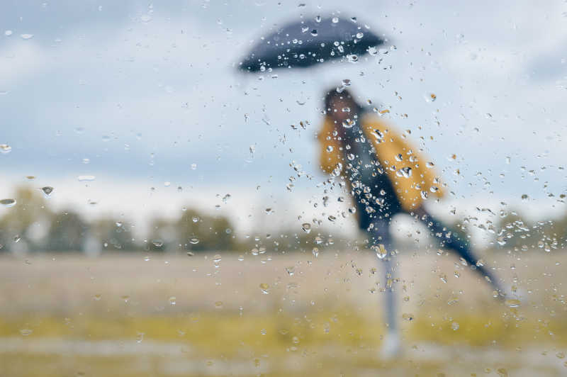 下雨淋有雨滴的窗户后面的打着伞的女孩