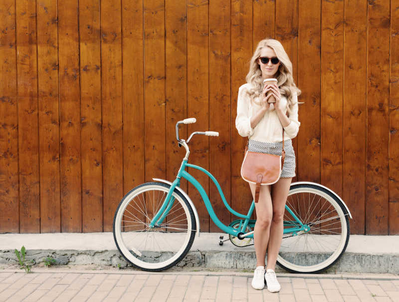 在自行车旁手拿咖啡戴着墨镜的女子