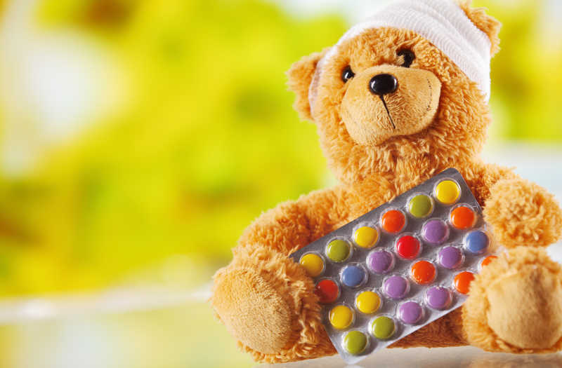 模糊背景下头缠绷带的玩具熊和彩色药丸
