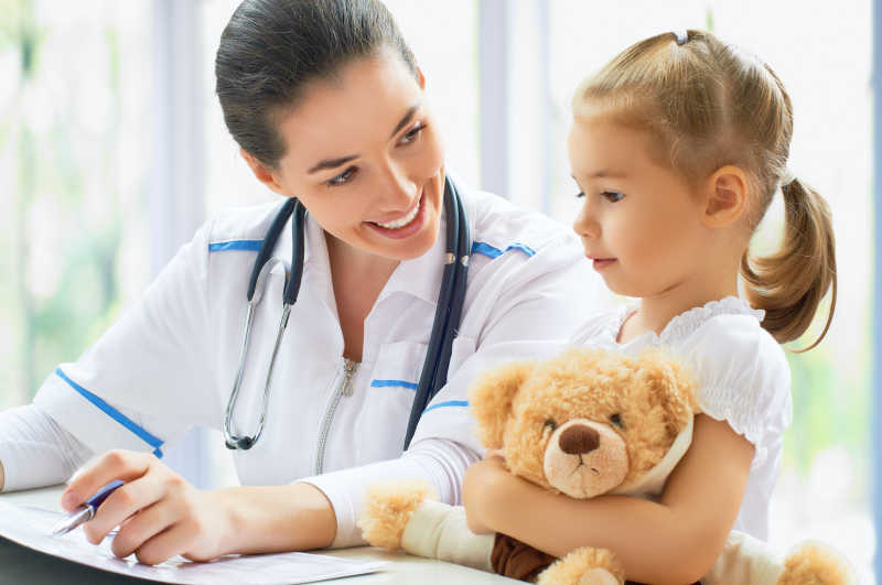 儿科医生为抱着玩具熊的女孩进行检查