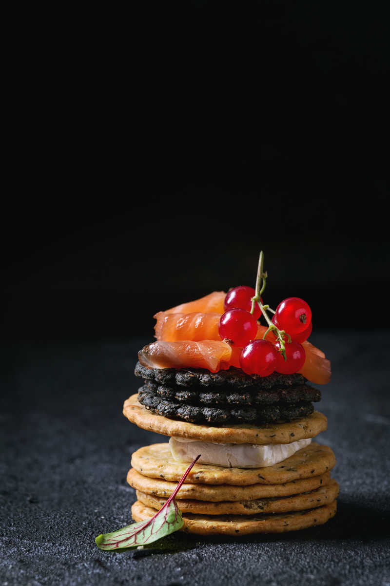 黑色背景下的饼干上放着三文鱼和红醋栗浆果