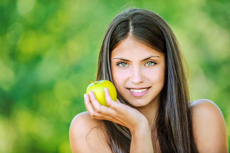 绿色背景下微笑的黑发美女手里拿着苹果
