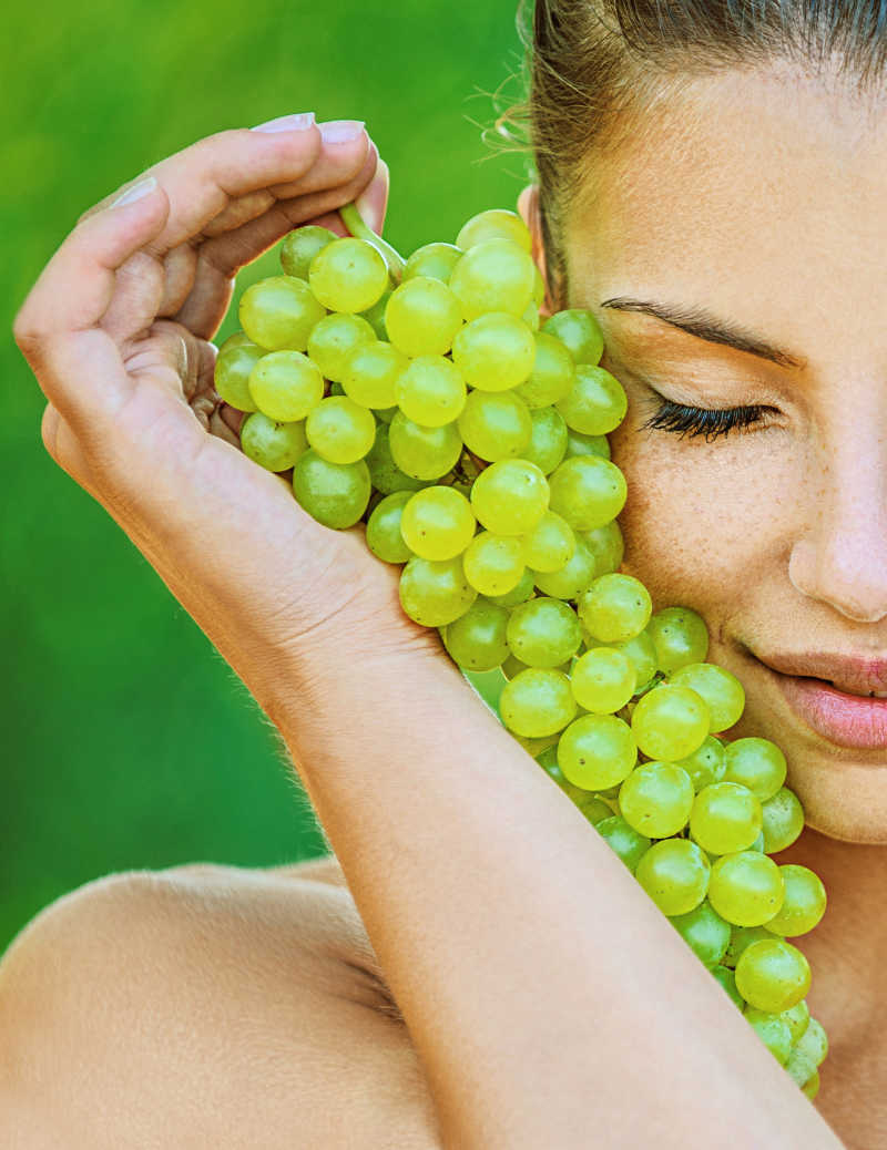 绿色的背景下美女抱着葡萄放在脸庞边上