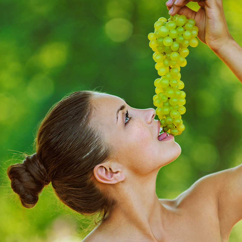 绿色背景下年轻美女正在吃手拿着的葡萄