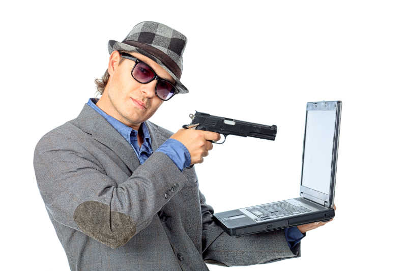 英俊的商人拿枪指着笔记本电脑