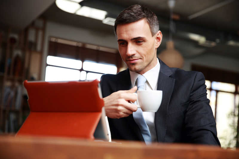 商人边喝咖啡边用平板电脑阅读消息