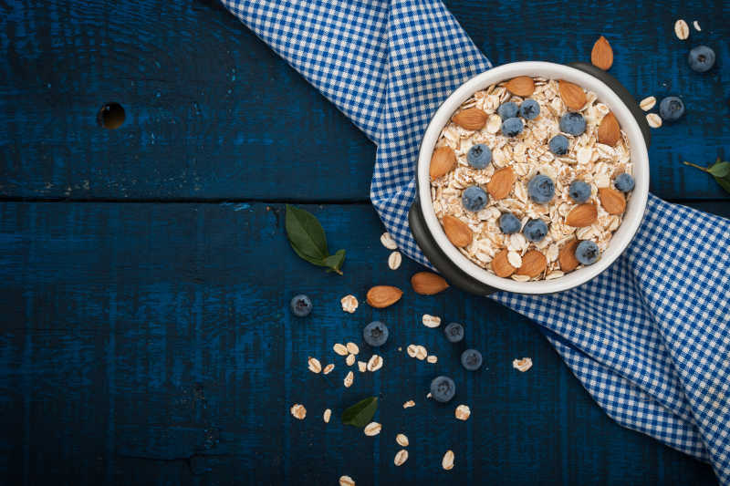 深蓝色木质背景的健康早餐燕麦片牛奶蓝莓蜂蜜和杏仁
