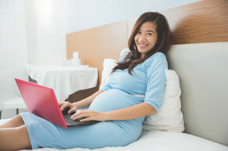 躺在床上的孕妇使用笔记本电脑