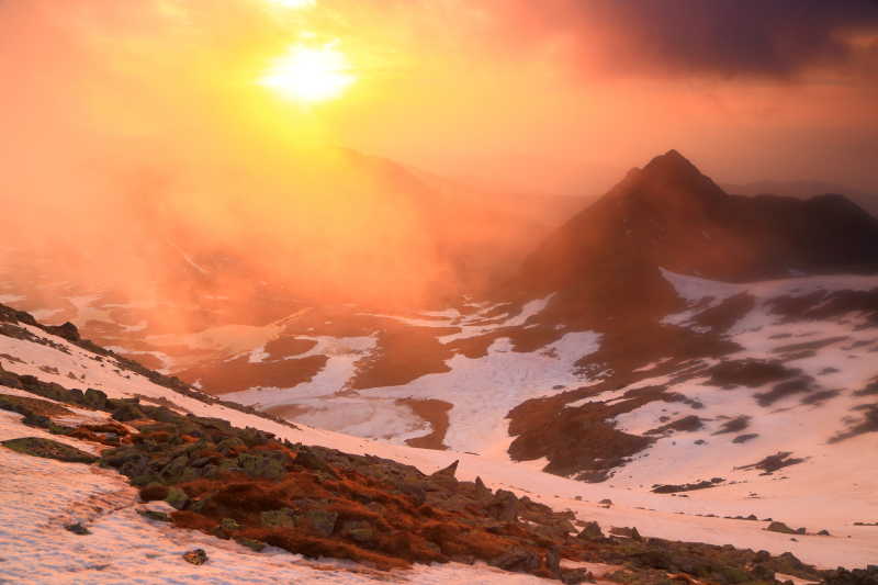 太阳穿透雪山上空的橙色云彩