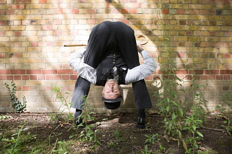 马戏团男子在砖墙边上展示颠倒的柔术