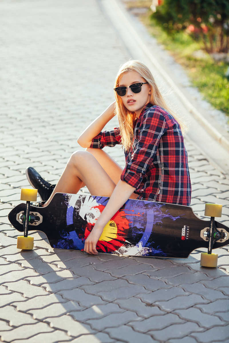 阳光下拿着滑板坐在地上的时尚女孩
