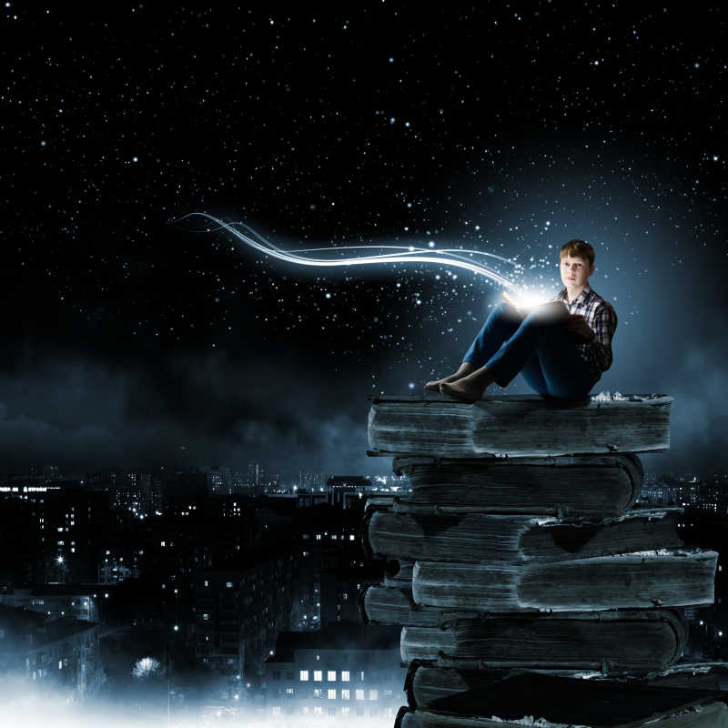 星空下坐在厚厚的书籍上看书的男孩