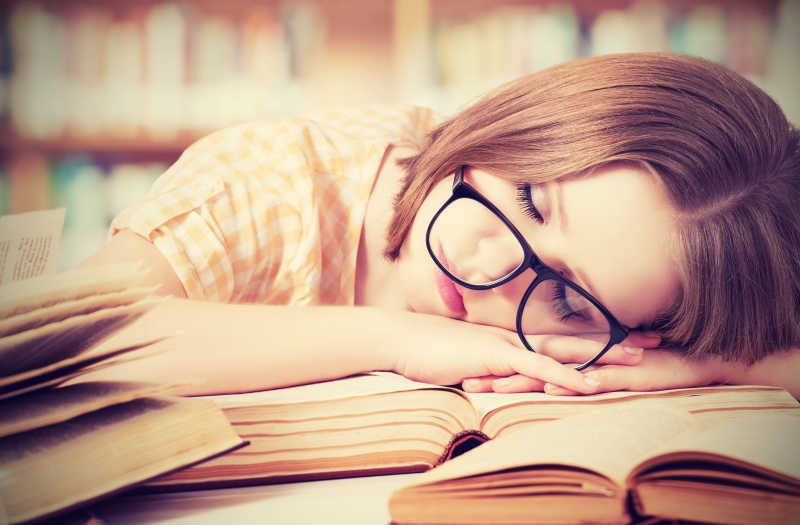 戴着眼镜趴在图书馆书桌上睡觉的女孩
