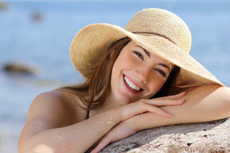 海边背景下趴在岩石上戴着太阳帽微笑的美女