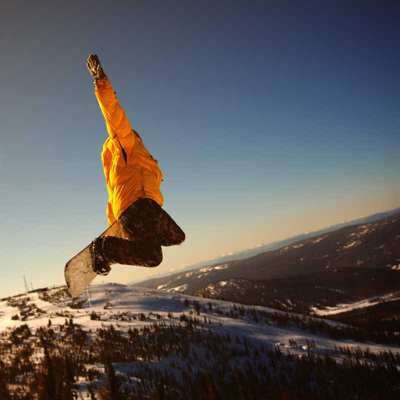 晴天山峦背景下跳跃起来的单板滑雪运动员