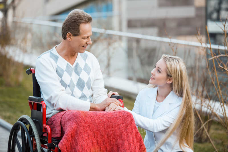 在户外坐着轮椅的成年男子和微笑的护士
