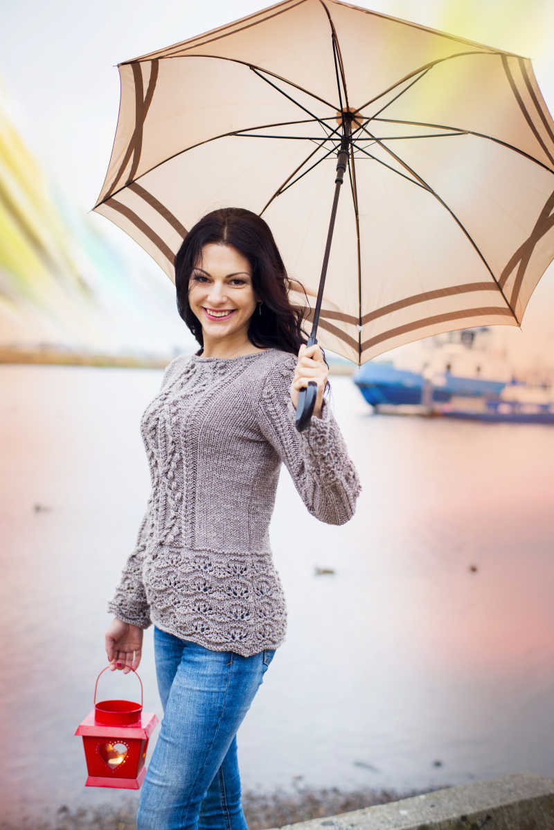 微笑的女人打着雨伞走在河边