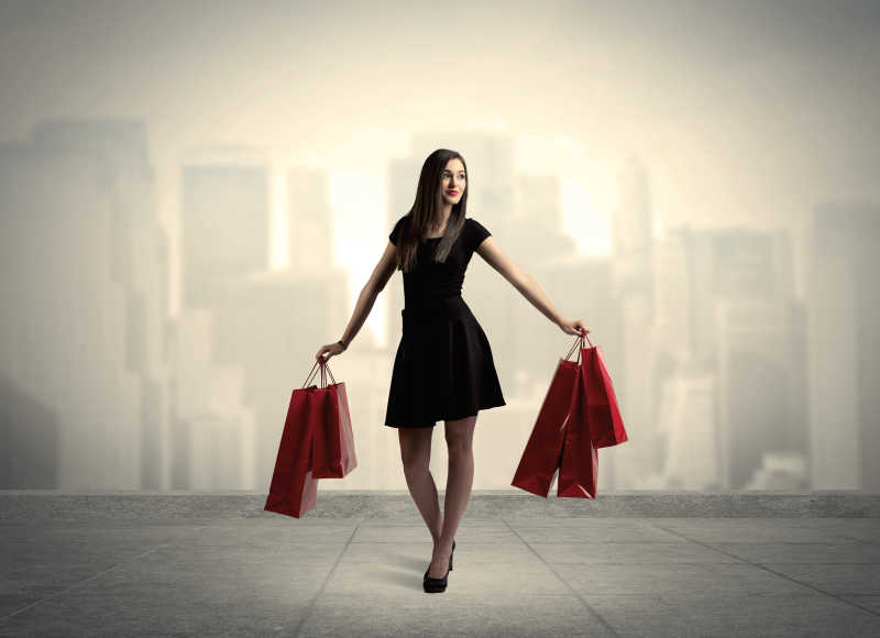 一个时尚的女性站在红色的购物袋在平台和城市景观背景概念