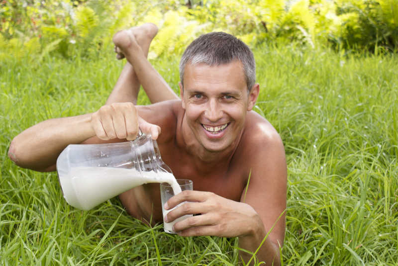 趴在野外草地上的中年男子正在倒牛奶