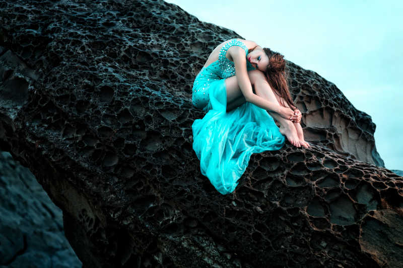 穿着长裙坐在海边岩石上的性感美女