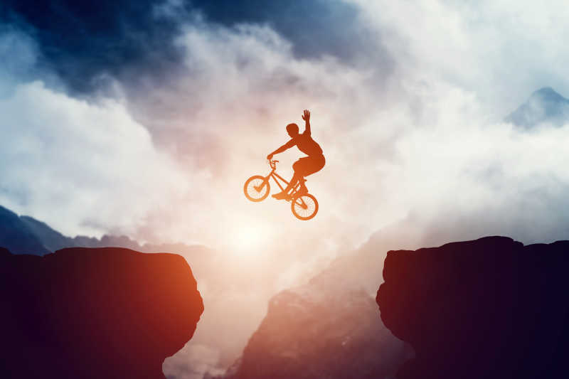 男子BMX自行车在山区日落跳悬崖