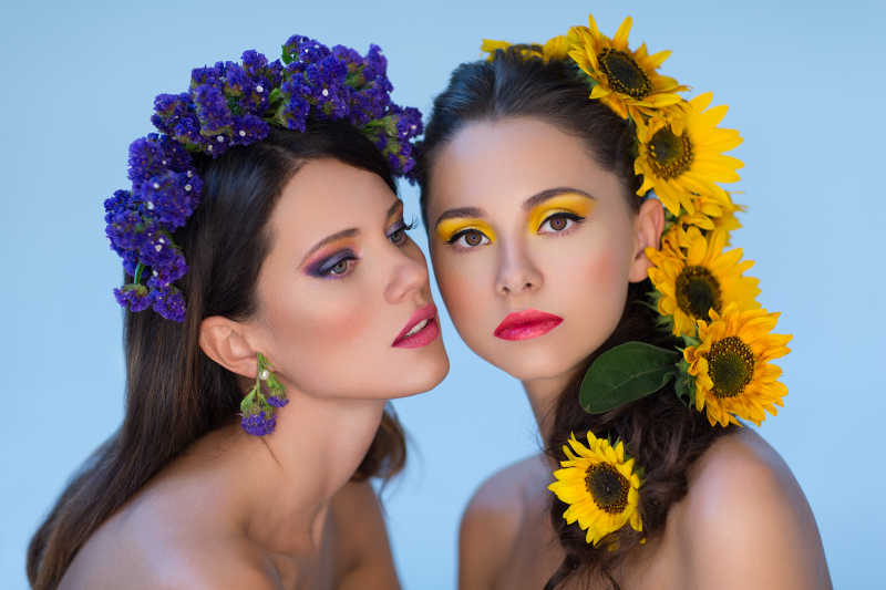 蓝色背景下头发上有黄色和紫色的花朵的两位美女