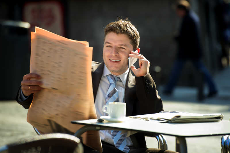 看着报纸高兴的用手机交谈的男商人