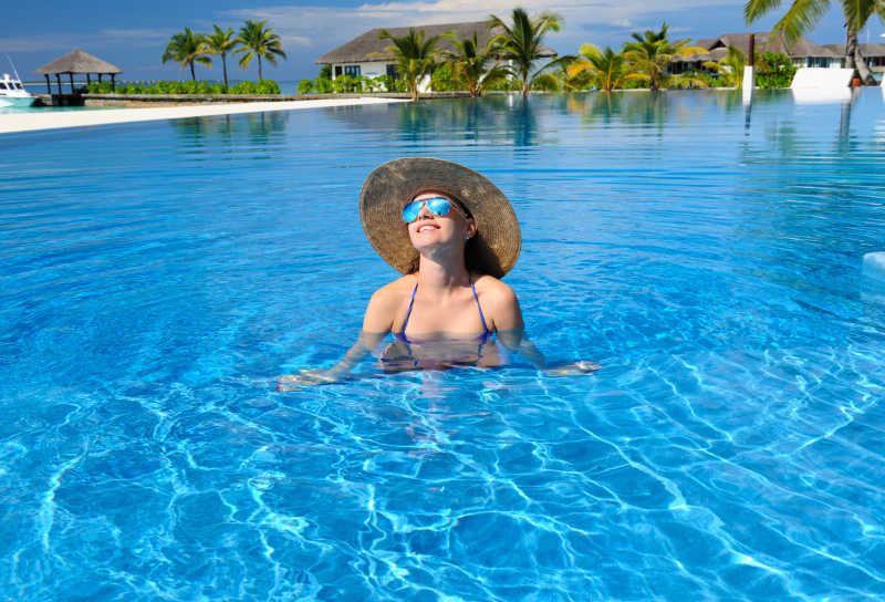 戴着太阳帽眼镜的微笑女人在度假村游泳池中