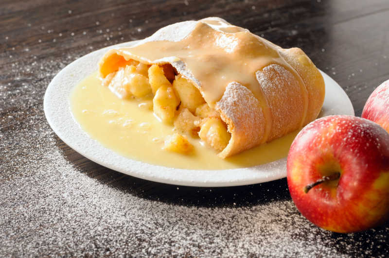 木桌上的白色盘子里的金黄色的馅饼和苹果
