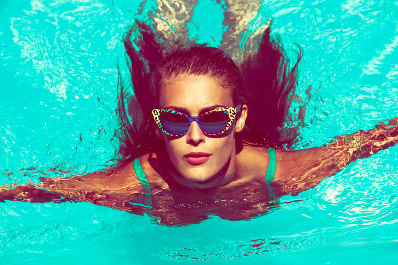 年轻漂亮的女子戴着太阳镜在游泳池内
