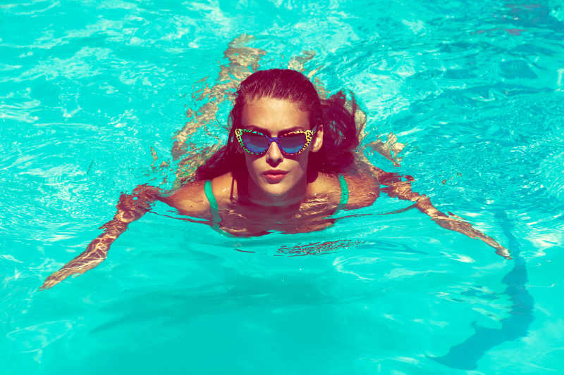 年轻漂亮的女子游泳池内戴着太阳镜在游泳