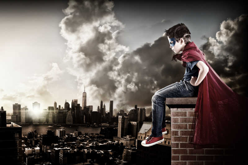 坐在高处的超级英雄男孩俯视着整个城市