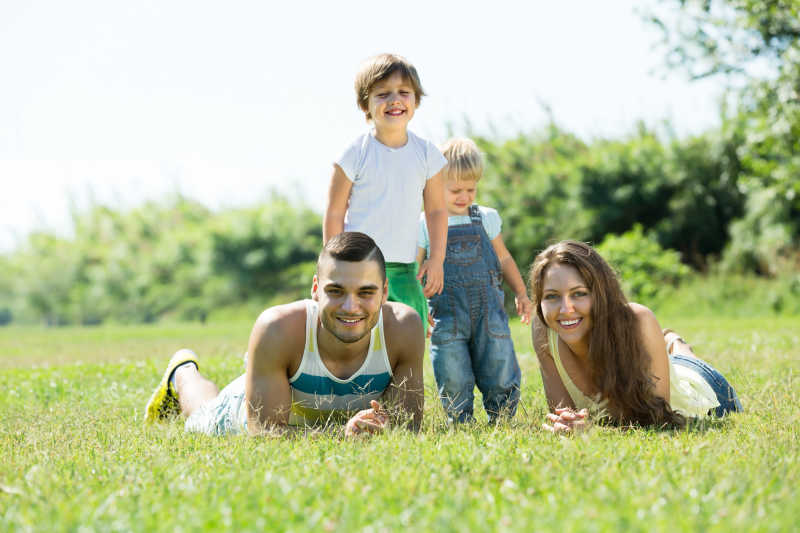 躺在草地微笑着的年轻父母和两个孩子