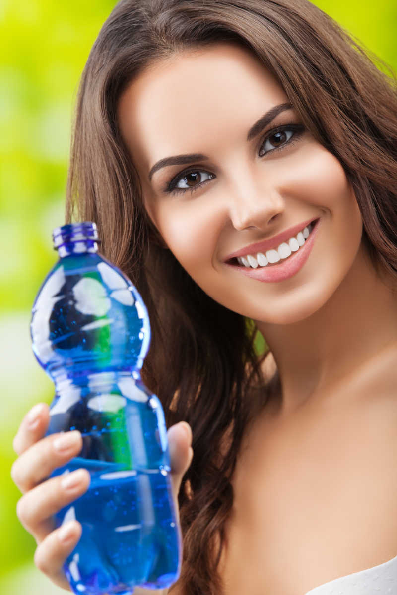 面带微笑的女人在户外展示着一瓶水