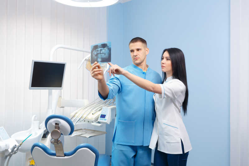 男性牙科医生和女性助理在牙科诊所看X光照片