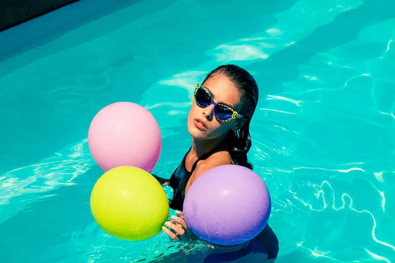 泳池里戴着太阳镜拿着气球的美女