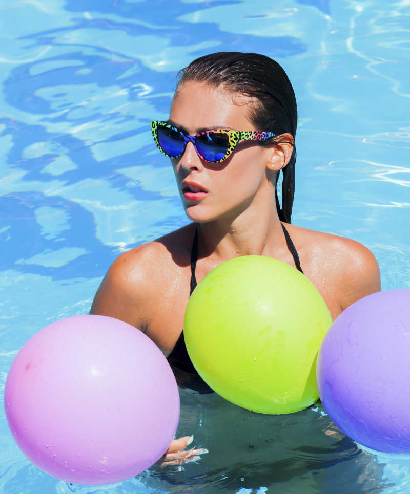 泳池里拿着彩色气球的性感比基尼美女