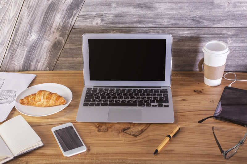 木桌上的笔记本电脑手机眼镜和面包