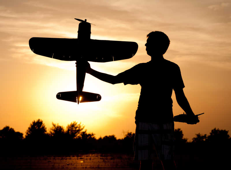 日出-日落背景下拿着飞机模型的年轻人剪影