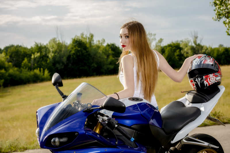 户外绿色植物背景下坐在蓝色摩托车上的年轻女子