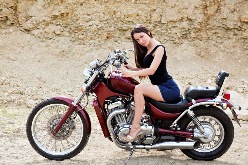 沙漠背景下骑着红色摩托车的年轻性感女子