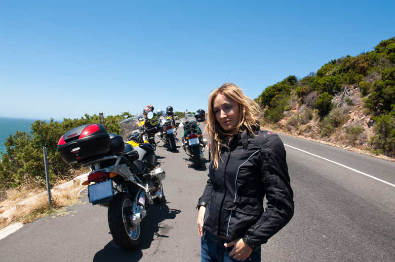 蓝天下山间公路上的摩托车队和黑衣年轻女子